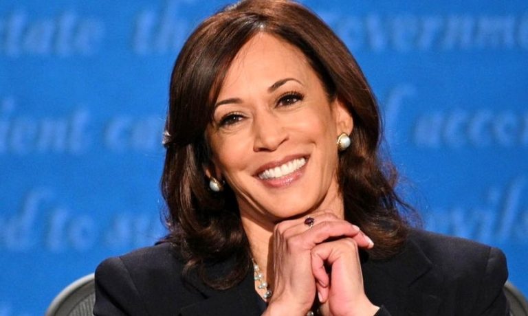 Kamala Harris nagyon örül a képen, kezeit egymásba kulcsolja és sötét blézert visel.