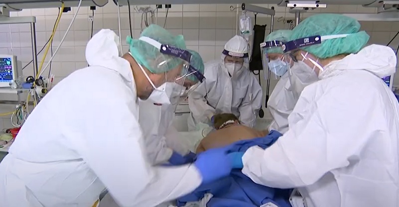 Öt szkafanderes, fehér védőruhás egészségügyi szakember kezel egy koronavírus-fertőzöttet a Honvédkórház egyik kórtermében.