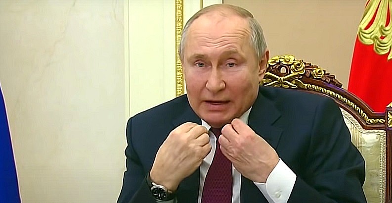 Vlagyimir Putyin idegesen, mutogatva magyaráz kék zakóban, fehér ingben és vörös nyakkendőben, miközben ül.