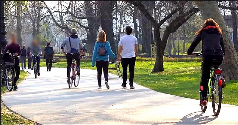 napsütésben sétál több ember az előtérben biciklizik egy nő