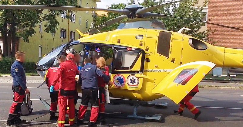 Sárga színű mentőhelikopterbe szállnak be az Országos Mentőszolgálat munkatársai egy zöld színű panelház mellett.
