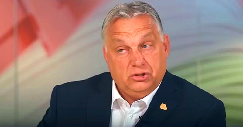 Orbán Viktor furcsán néz és ráncolja a homlokát, miközben arca barnássárga színű. Zakója sörétkék, ingje fehér, kitűző van rajta. (Zobori Élménypark)