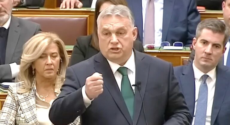 Orbán Viktor sötétkék zakóban, fehér ingben, zöld nyakkendőben ökröt rázva, mutogatva beszél az Országgyűlés alsóházi üléstermében.