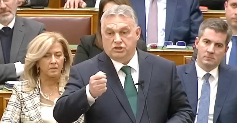 Orbán Viktor sötétkék zakóban, fehér ingben, zöld nyakkendőben ökröt rázva, mutogatva beszél az Országgyűlés alsóházi üléstermében.