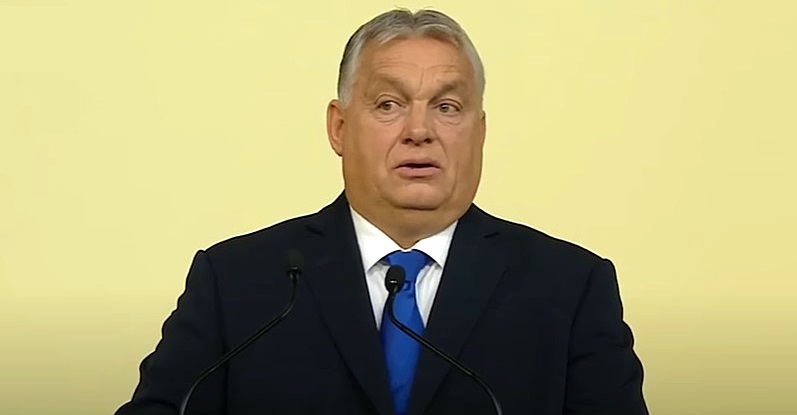 Orbán Viktor, sárga fal, fekete öltöny, fehér ing, kék nyakkendő