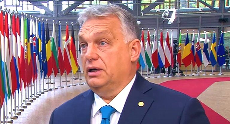 Orbán Viktor kék zakóban, fehér ingben, világoskék nyakkendőben meglepetten beszél az Európai Tanács helyszínén.