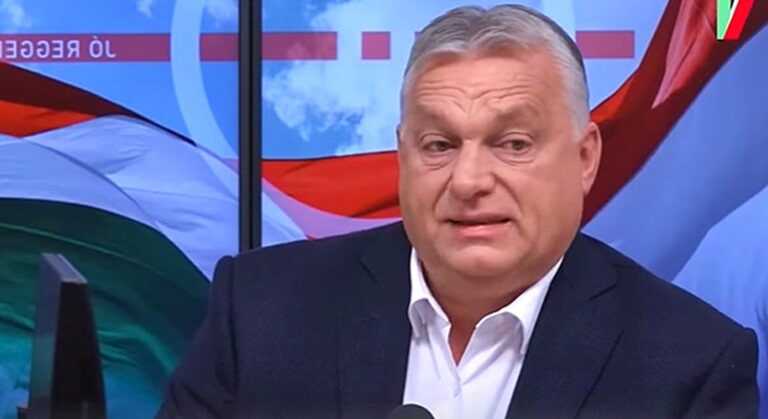 Orbán Viktor fehér ingben, fekete öltönyben egy mikrofon előtt beszél