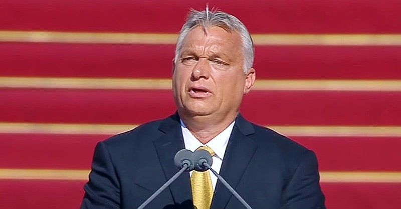 Orbán Viktor piros háttér előtt beszél egy mikrofonba