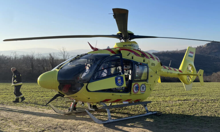 Az Országos Mentőszolgálat citromsárga színű mentőhelikoptere látható a képen egy pusztaságban.
