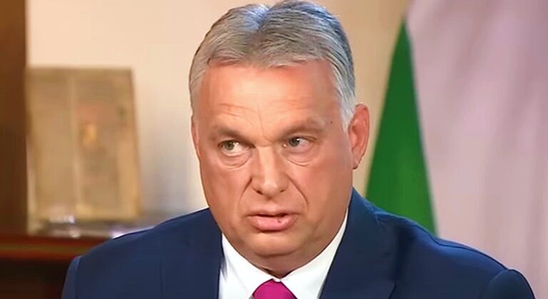 Orbán Viktor kék zakóban, fehér ingben és vörös nyakkendőben látható, amint furcsán grimaszol.