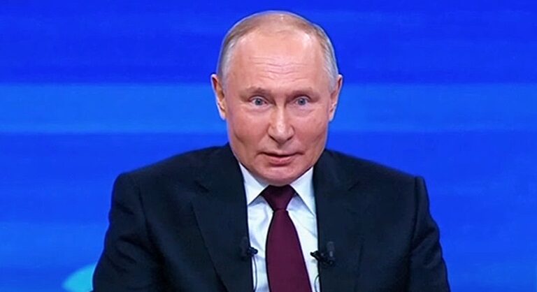 Vlagyimir Putyin sötét színű zakóban, fehér ingben, bordó nyakkendőben furcsán néz