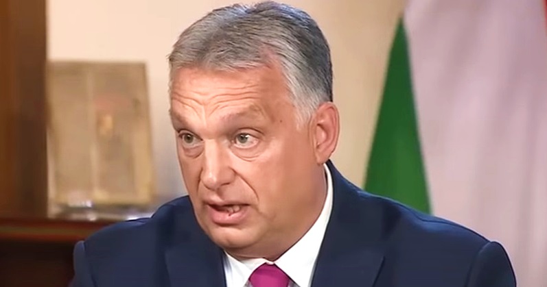 Orbán Viktor kék zakóban, fehér ingben, vörös nyakkendőben, ősz hajjal meglepetten néz a kamerába.