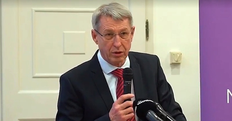 Hartmann Ferenc beszédet mond fekete öltönyben piros nyakkendőben egy mikrofon előtt