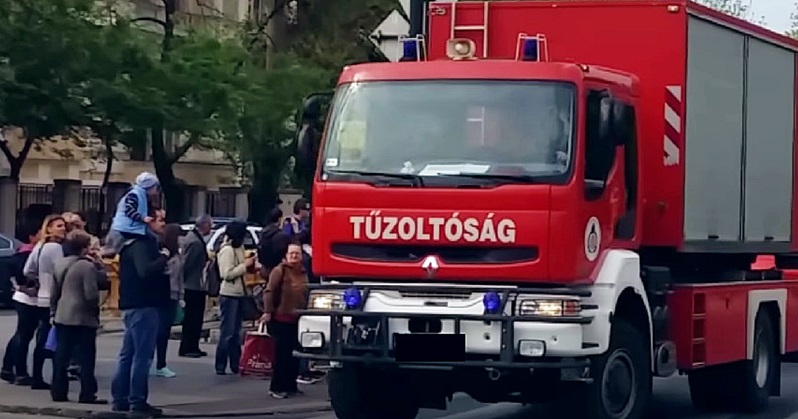 Tűzoltóautó siet a tűzoltókkal tűzhöz, emberek állnak körülötte