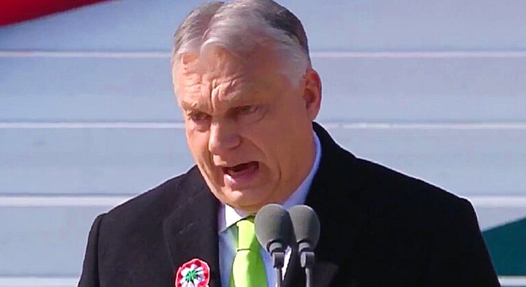 Orbán Viktor március 15-én, fekete öltönyben, fehér ingben, a zöld nyakkendőben a mikrofon előtt