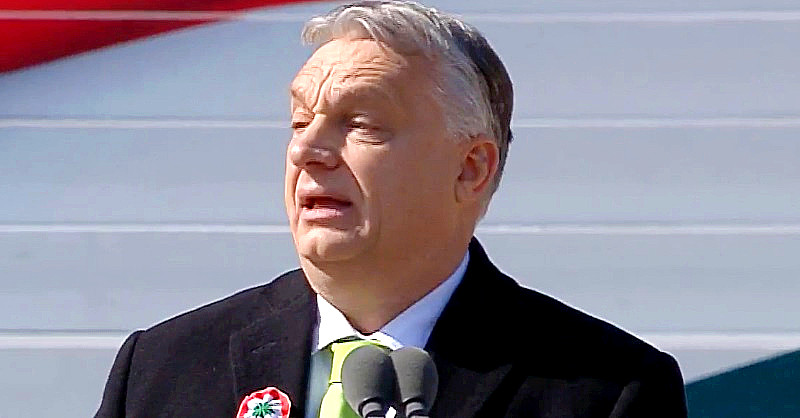 Orbán Viktor rövid, ősz hajjal kissé illuminált tekintettel mered magaelé. Rajta fekete zakó, fehér ing és zöld nyakkendő látható, zakóján pedig kokárda van.