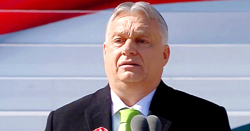 Orbán Viktor fekete zakóban, fehér ingben, zöld nyakkendőben és kokárdában mond megszeppenten beszédet március 15-én.