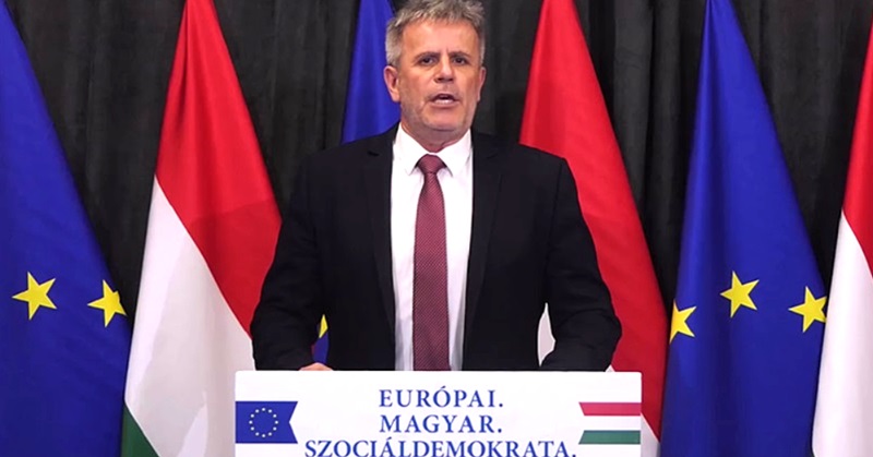 Varga Zoltán DK sajtótájékoztató, beszéd, fekete öltöny, fehér ing, piros nyakkendő