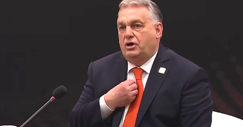 Orbán Viktor kanapén, fekete öltönyben, fehér ingben, narancssárga nyakkendőben