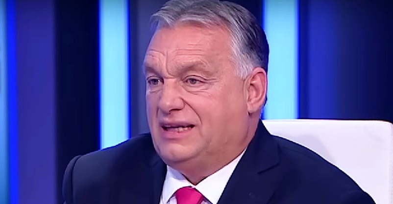Orbán Viktor kék háttér előtt, sötétkék öltönyben, piros nyakkendőt visel, interjút ad egy stúdióban