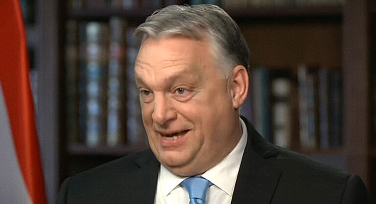 Orbán Viktor fekete zakóban, fehér ingben, kék nyakkendőben, ősz hajjal furcsán néz a kamerába.