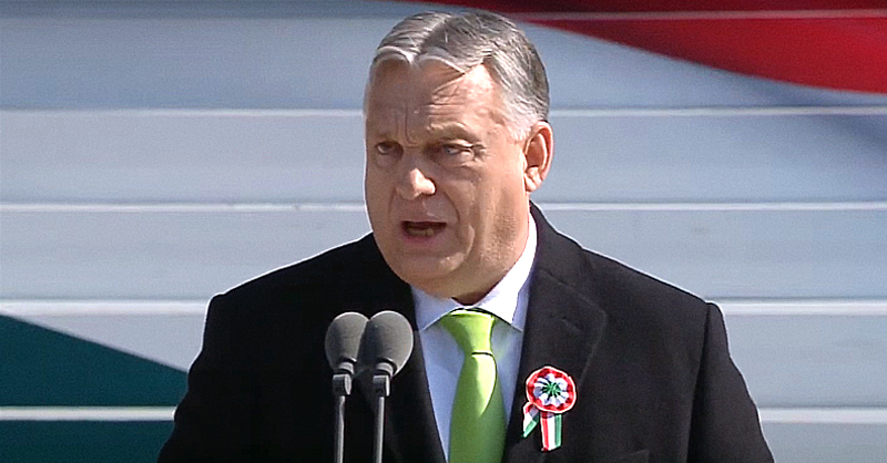 Orbán Viktor fekete zakóban, fehér ingben és zöld nyakkendőben szónokol; zakóján kokárda van. Haja ősz, homloka ráncos, és furcsa fejet vág beszéde közben.