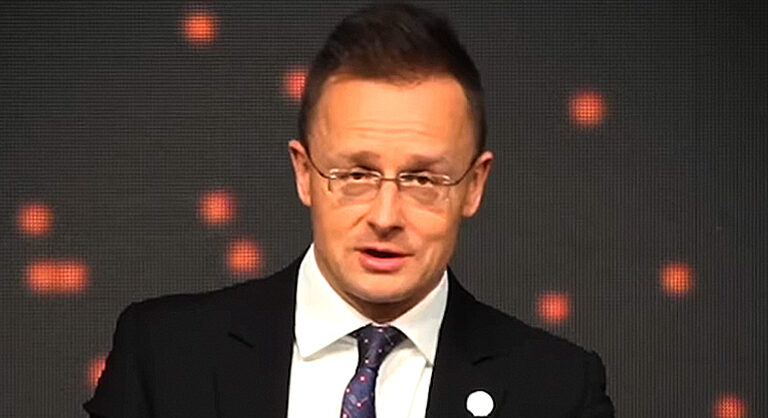 Szijjártó Péter külgazdasági és külügyminiszter szemüvegben rövid hajjal néz fehér ingben