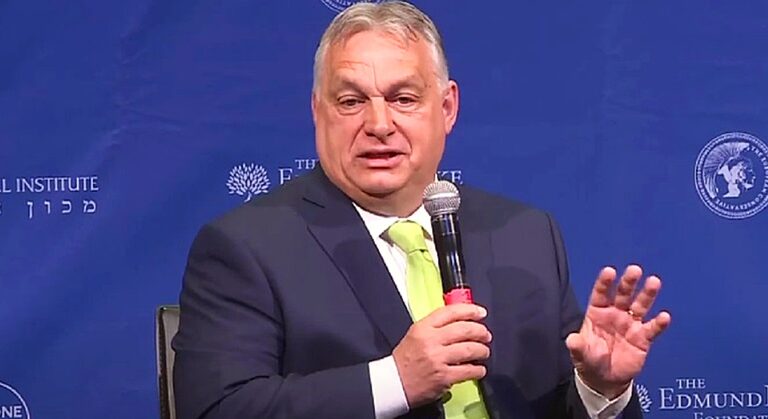 Orbán Viktor, mikrofon, kék háttér, fekete öltöny, fehér ing, zöld nyakkendő