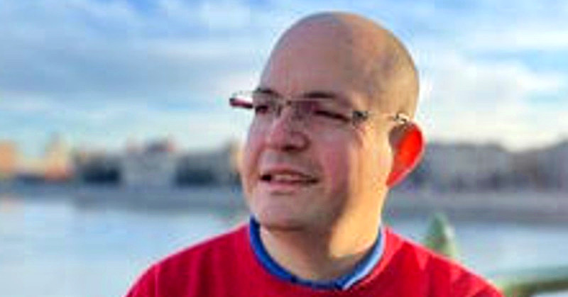Tőke Márton kopaszon, szemüvegben, piros pulcsiban egy hídon áll.