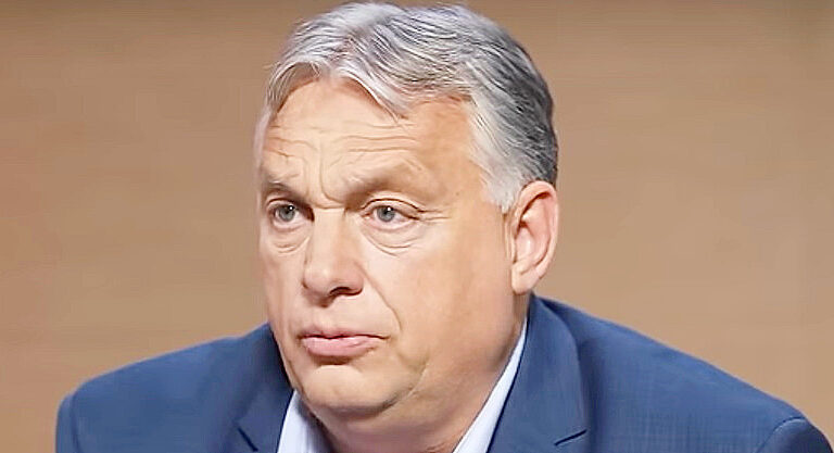 Orbán Viktor sötétkék zakóban, fehér ingben, ősz hajjal, ráncos homlokkal rémülten néz, miközben beszél. A háttér barna színű.