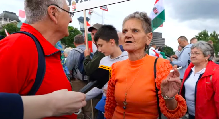 Békemeneten narancssárga ruhás nő cigivel a kezében nyilatkozik az index mikrofonjának