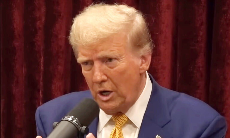 Donald Trump kék zakóban, fehér ingben, sárga pöttyös nyakkendőben beszél, miközben balra néz rémült tekintettel.