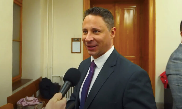 Schadl György egy mikrofonba beszél dühösen a bíróságon, a háttérben a tárgyaló ajtaja