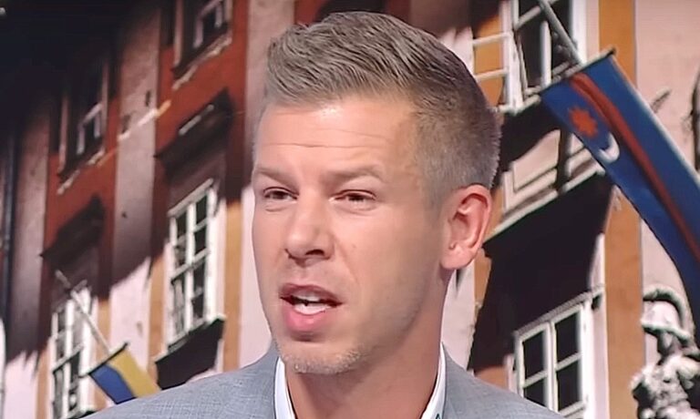 Magyar Péter szürke zakóban, fehér ingben, őszülő szőke hajban grimaszol, miközben enyhén balra néz.