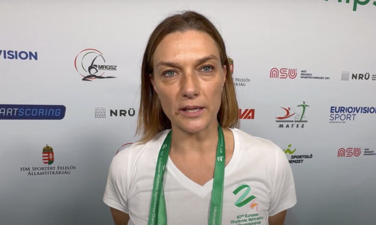 Deutsch-Lazsányi Erika fehér pólóban és fehér hirdetőtábla előtt beszél