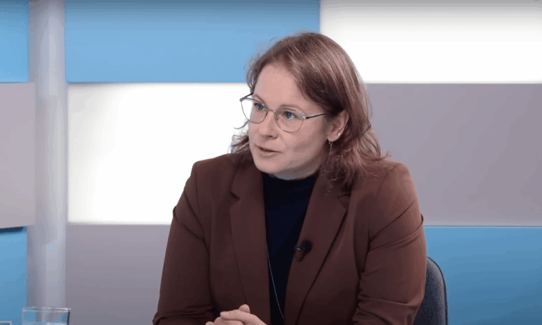 Keszthelyi Dorottya barna zakóban és fekete felsőben interjút ad egy világos stúdióban