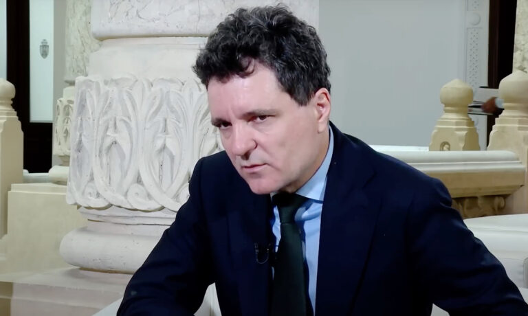 Nicusor Dan öltönyben beszél egy fehér oszlop előtt
