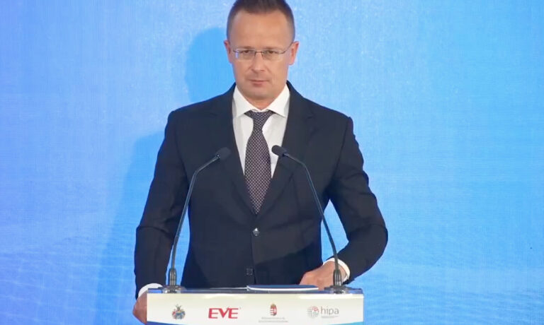 Szijjártó Péter az Eve Power akkumulátorgyár bejelentésén kék háttér előtt beszél két kis mikrofonba