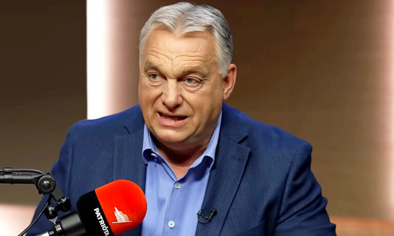 Orbán Viktor sötétkék zakóban, világoskék ingben, ősz hajjal, meggyötört arccal enyhén balra nézve a mikrofonba beszél.