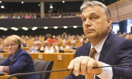 Orbán Viktor öltönyben, fehér zakóban, barnássárga nyakkendőben a mikrofont fogja az Európai Parlament üléstermében.