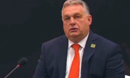 Orbán Viktor fekete háttér előtt, sötétkék öltönyben, narancssárga nyakkendőben