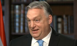 Orbán Viktor fekete zakóban, fehér ingben, kék nyakkendőben, ősz hajjal furcsán néz a kamerába.