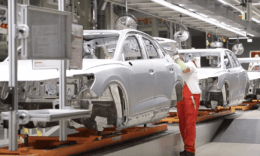 A győri Audi-gyárban egy piros ruhás munkás rak össze egy fehér vázú Audit a gyártósoron