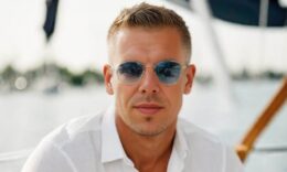 Magyar Péter fehér ingben napszemüvegben ül egy hajón a háttérben víz